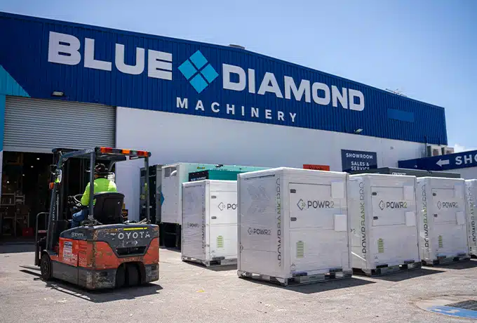 Worker driving by a fleet of POWRBANK POWR2 energy storage systems outside Blue Diamond Machinery's warehouse.