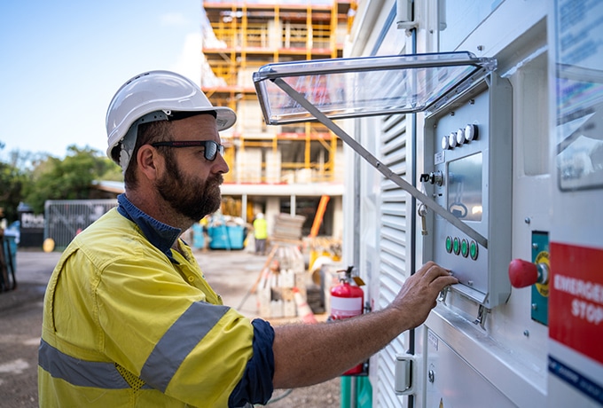 Blue Diamond Machinery worker operating the equipment monitoring system of an AMPD ESS unit on a construction site.